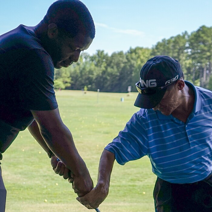 Marty Turcios guiding a participant's grip on the golf club, hands together at a driving range