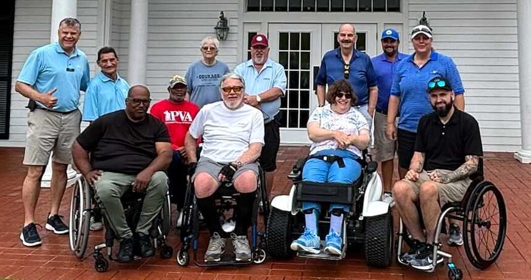 A group of MTTG clinic participants and volunteers, several using wheelchairs, gathered together at a golf clubhouse